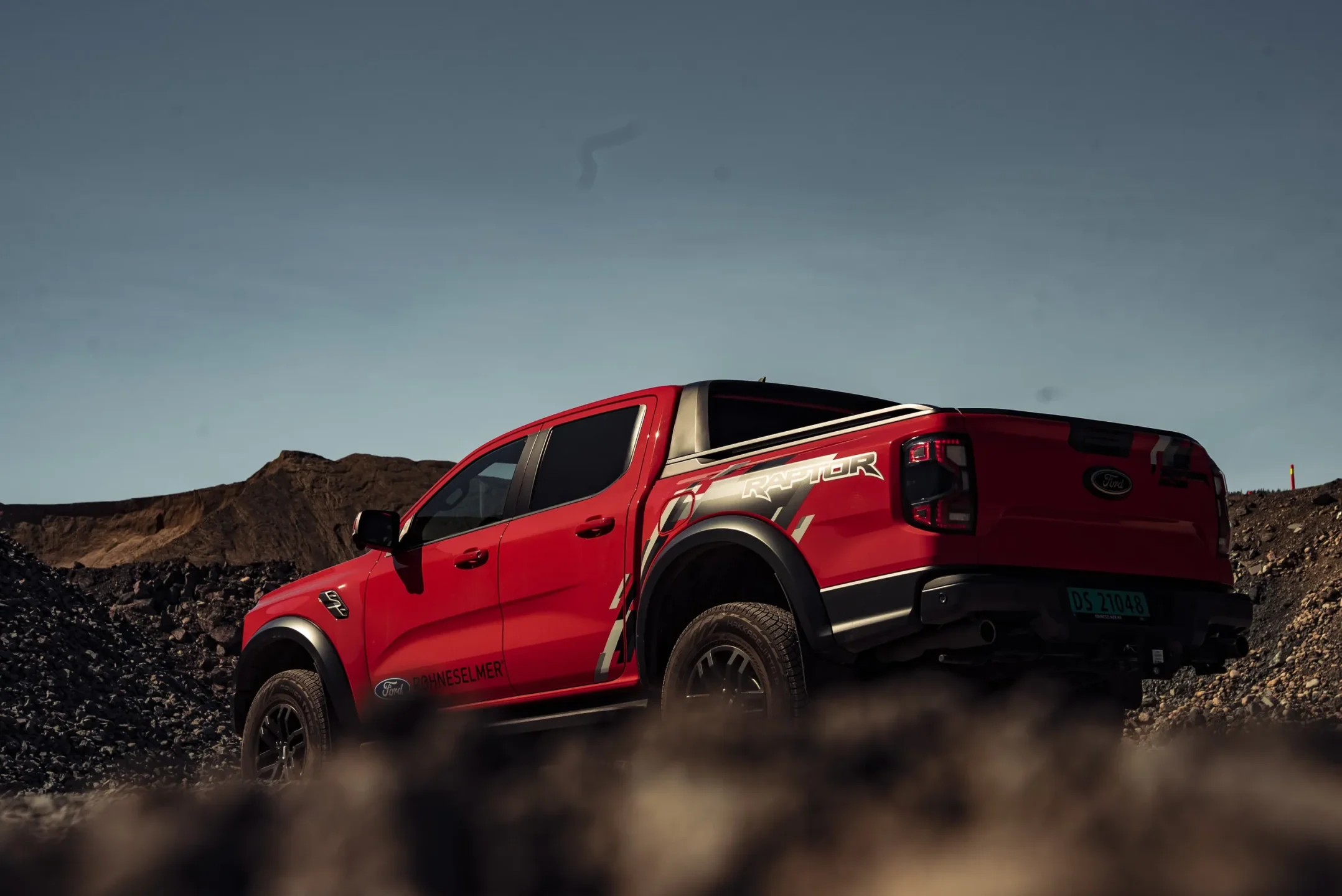 Rød pickup med offroad-dekk fotografert i et grustak i lavt kveldslys