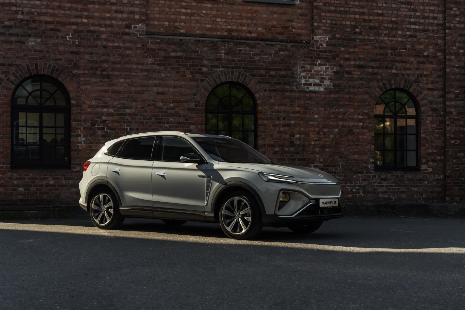 Lys SUV parkert foran murbygg med buede vinduer i kveldslys