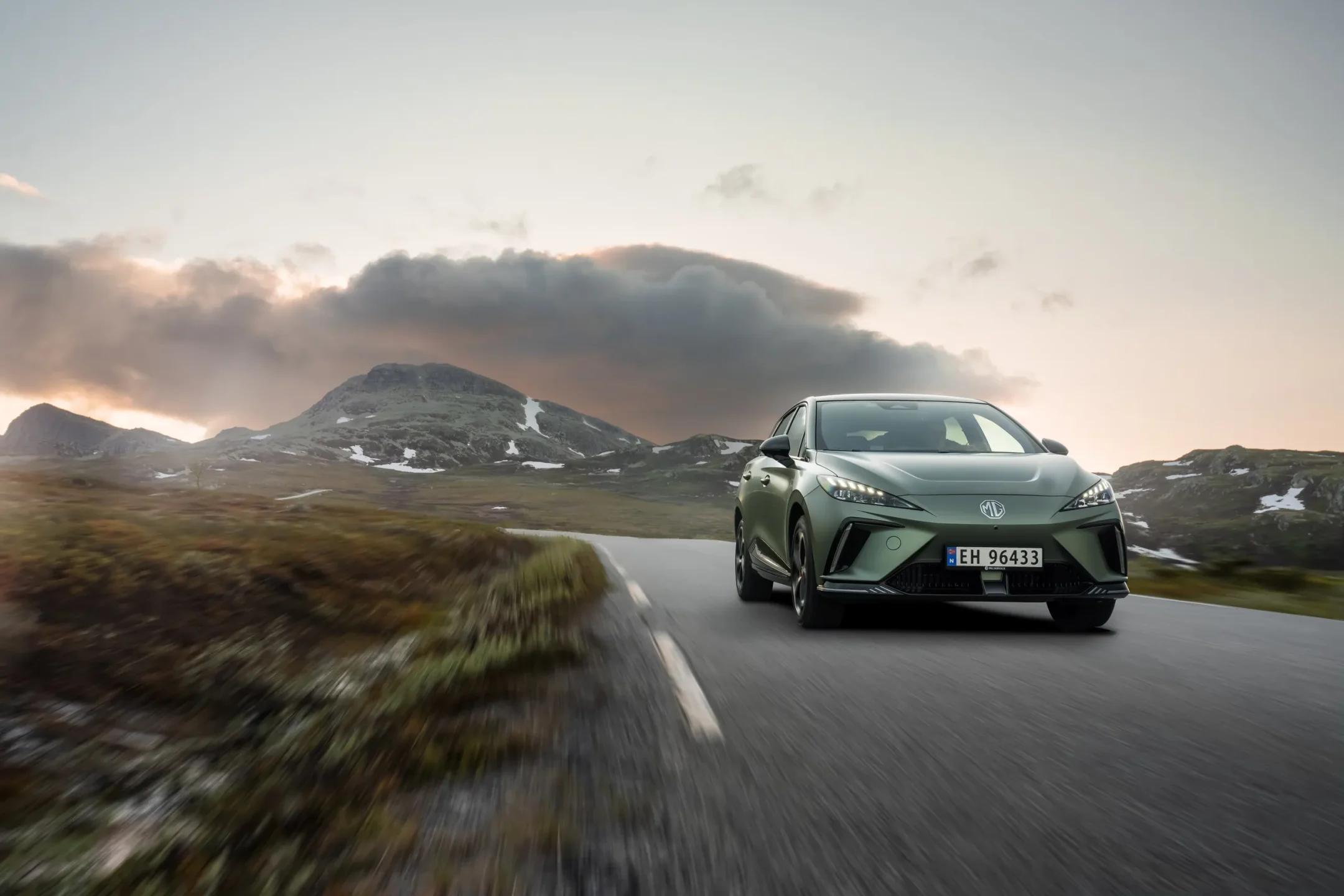 Grønn elbil-SUV i fart på fjellvei ved solnedgang